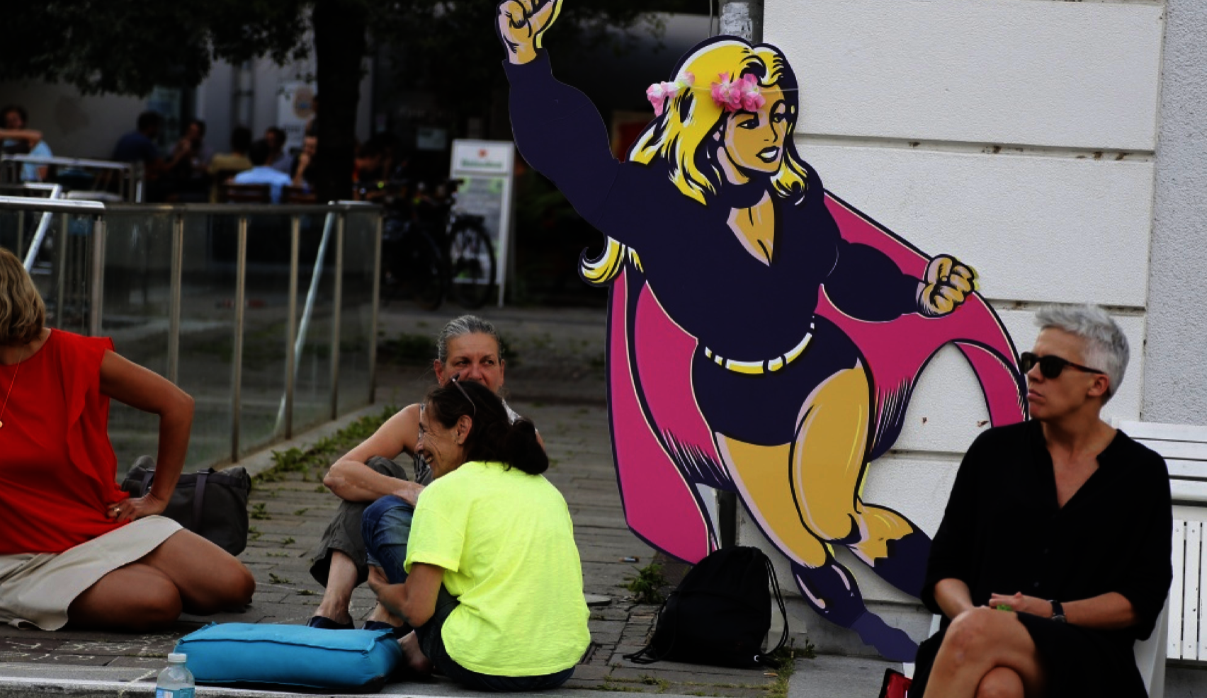 Einige Frauen sitzen um eine große Pappfigur und unterhalten sich. Die Figur zeigt das Logo des Womens Action Forums.