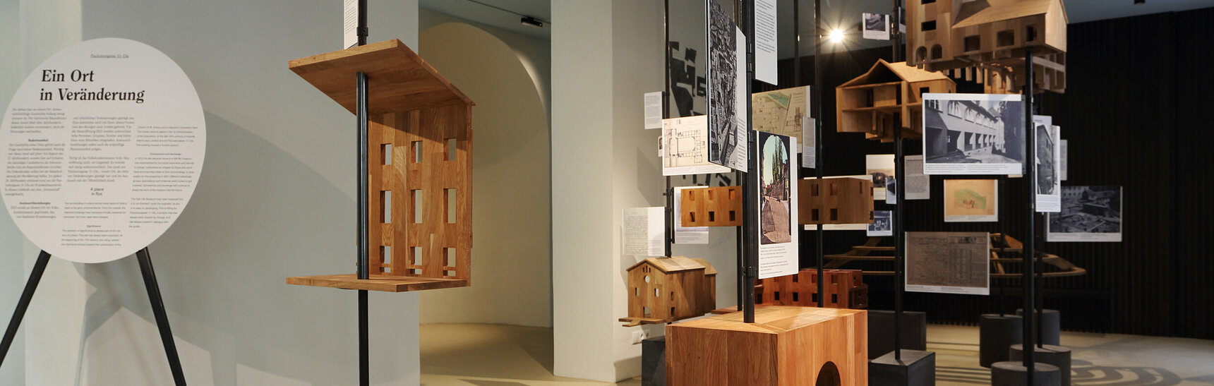 Ausstellungsansicht: Modelle aus Holz der verschiedenen Bauteile des Museumsareals, schwebend angebracht an Metallstangen.