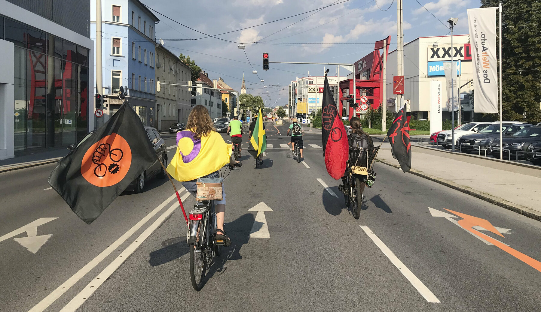 Teilnehmerinnen des Critical Mass fahren mit ihren Fahrrädern auf der Straße. Sie sind dabei mit Flaggen geschmückt und nehmen die gesamte Straße ein.