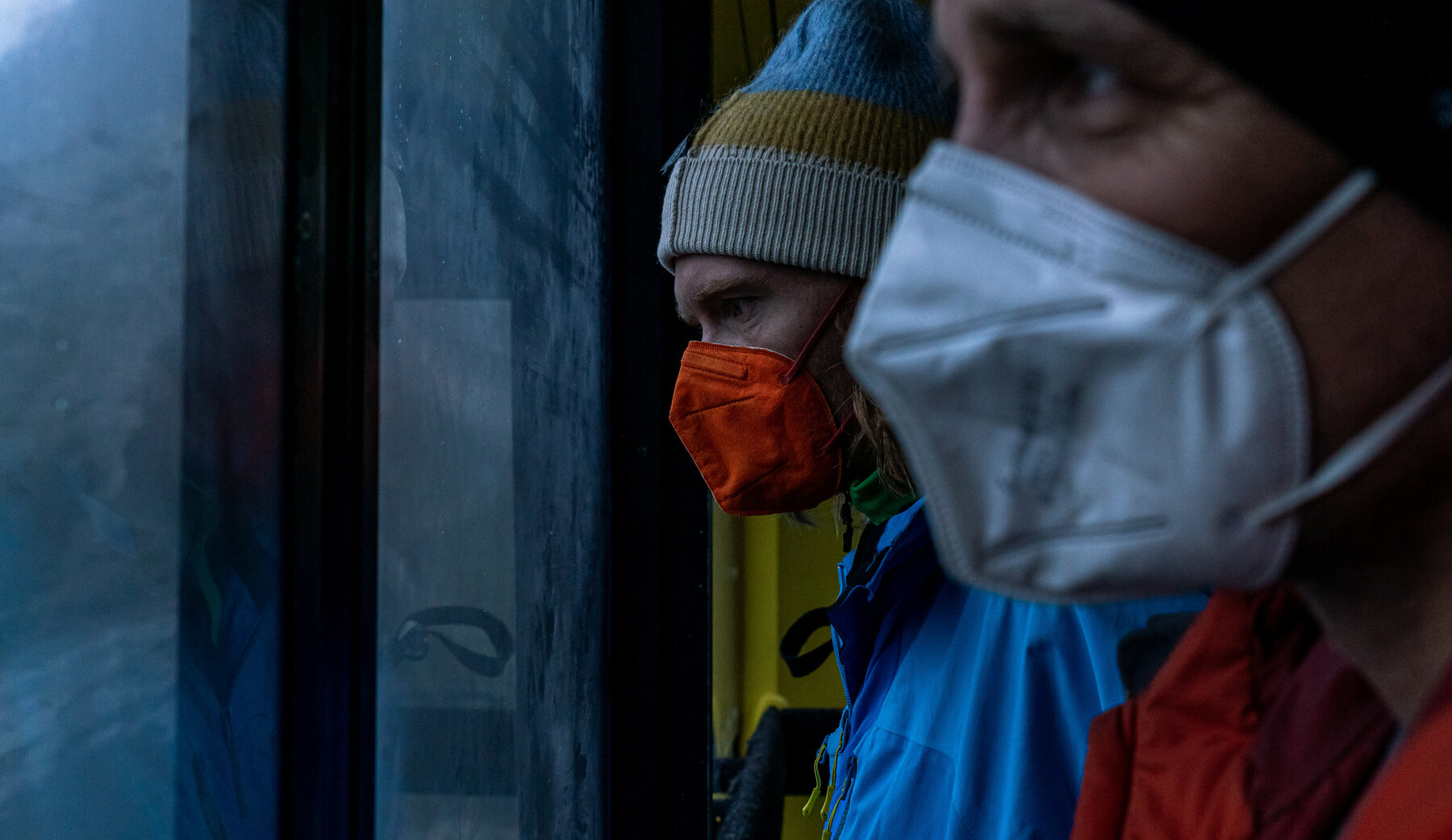Zwei Männer mit Mund Nasen Schutz und dicker Winterkleidung in Nahaufnahme schauen aus dem Fenster der Gondel am Dachstein