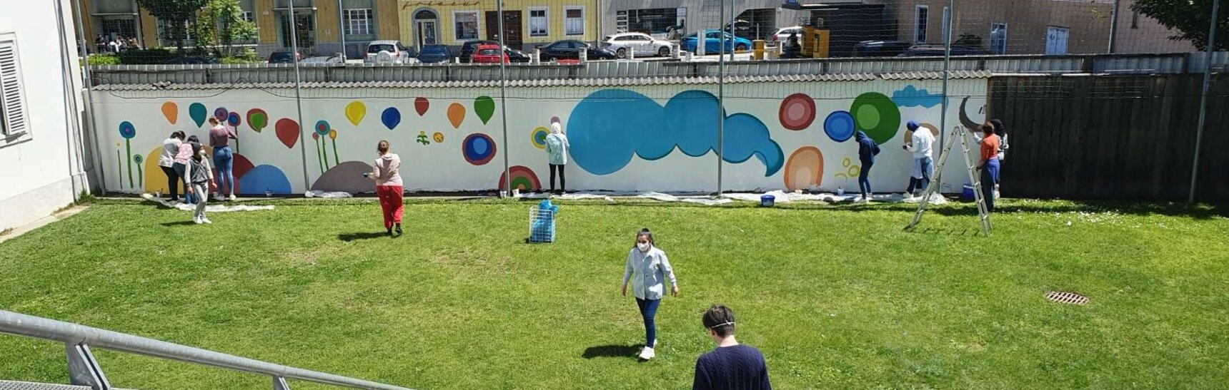 Ansicht des Schulhofes der Mittelschule St. Andrä in Graz. Die Kinder und die Künstlerinnen sind dabei die Mauern auszumalen